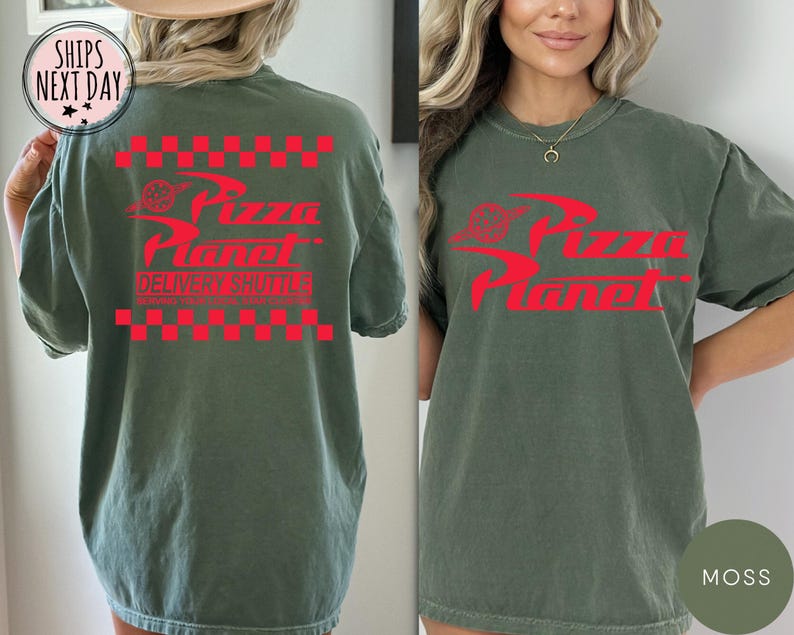 May include: A moss green t-shirt featuring a red Pizza Planet logo and text. The design includes a red checkered pattern above and below the logo, with the words "Delivery Shuttle" below. The shirt has a relaxed, oversized fit.