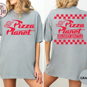 May include: A grey t-shirt with the red "Pizza Planet" logo on the front and back. The back of the shirt also features the text "Delivery Shuttle" and "Serving Your Local Star Cluster".