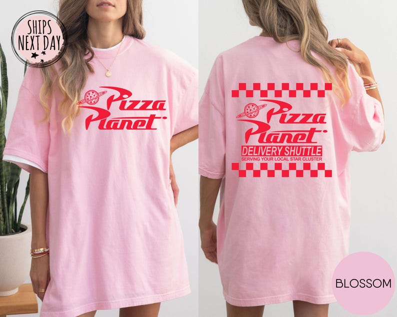 May include: A pale pink t-shirt featuring the Pizza Planet logo in red on the front and back. The back of the shirt also displays the text "DELIVERY SHUTTLE" and "SERVING YOUR LOCAL STAR CLUSTER". The shirt has a white collar.