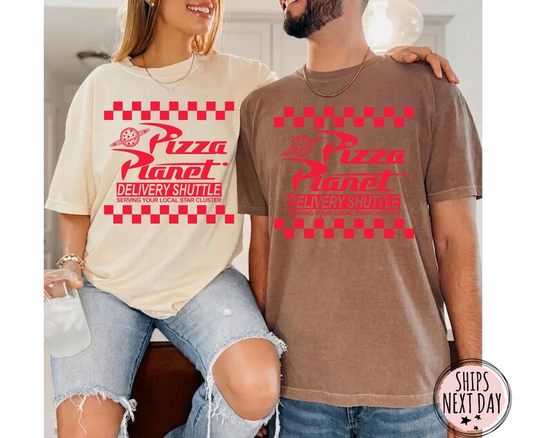 May include: Two short-sleeved t-shirts, one cream and one brown, display the Pizza Planet logo in red. The logo includes the text "Pizza Planet Delivery Shuttle Serving Your Local Star Cluster" in a red checkered pattern.