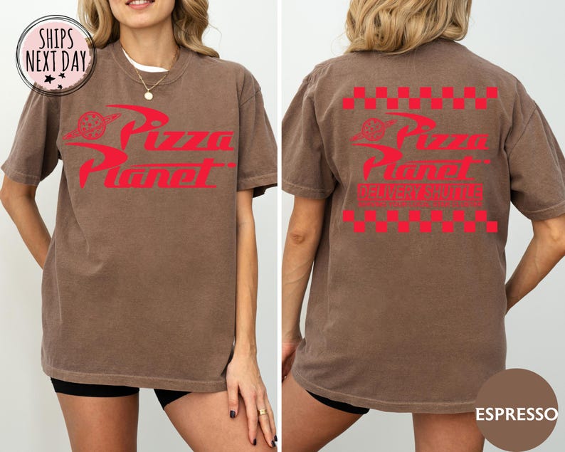 May include: A brown t-shirt with the Pizza Planet logo in red on the front and back. The front logo includes a pizza slice graphic, and the back has a red and white checkered pattern. The shirt is a casual, unisex style, in a brown colour.