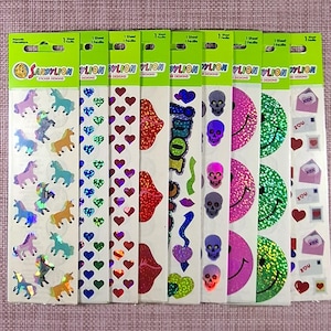 Könnte beinhalten: Acht vertikale Bögen mit Sandylion-Aufklebern, die verschiedene holografische und bunte Motive zeigen. Die Bögen enthalten Einhörner, blaue und rote Herzen, rote Lippen, violette Totenköpfe, rosa und grüne Smileys sowie Umschläge mit Herzen.
