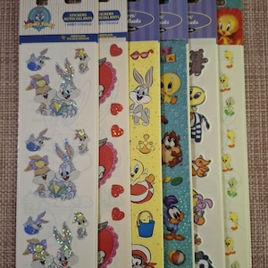 Puede incluir: Varias hojas de pegatinas de Looney Tunes con personajes como Bugs Bunny y Piolín. Las pegatinas son coloridas y tienen un efecto holográfico brillante. El embalaje incluye el texto "LOONEY TUNES" y "STICKERS AUTOCOLLANTS".