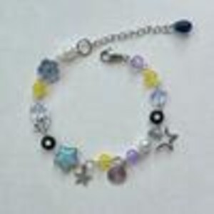 May include: A beaded bracelet with a silver chain and clasp. The bracelet features a variety of colorful beads, including yellow, blue, purple, and clear beads, along with star-shaped charms and a small, round charm. The bracelet is designed to be adjustable.