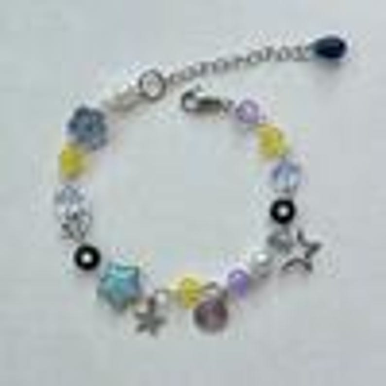 May include: A beaded bracelet with a silver chain and clasp. The bracelet features a variety of colorful beads, including yellow, blue, purple, and clear beads, along with star-shaped charms and a small, round charm. The bracelet is designed to be adjustable.