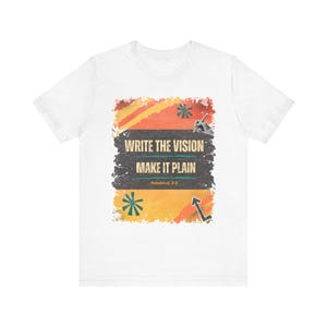 Könnte beinhalten: Ein weißes Kurzarm-T-Shirt mit einer zentralen Grafik auf einem abgenutzten orange-gelben Hintergrund. Der Text lautet "WRITE THE VISION" und "MAKE IT PLAIN" über "Habakkuk 2:2". Eine Hand mit Stift und abstrakte Formen sind abgebildet.