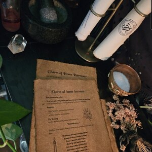 May include: An arrangement of spiritual items on a dark surface. Includes a mortar and pestle, a clear crystal, a small bottle, a metal stand holding rolled papers, a decorative bowl with salt, dried flowers, and aged paper with text: "Charm of Home Harmony."