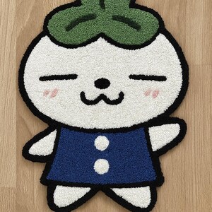 Può includere: Un tappeto stravagante a forma di personaggio dei cartoni animati con corpo bianco, abito blu e copricapo verde a forma di trifoglio. Il tappeto ha un contorno nero e guance rosa. Il tappeto è alto circa 61 cm e largo 46 cm.