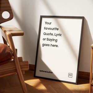 Könnte beinhalten: Ein gerahmter Druck mit schwarzem Rahmen, der an einer weißen Wand lehnt. Der Druck zeigt den Text "Your favourite Quote, Lyric or Saying goes here." Unter dem Text steht "Optional Author" und ein Logo.