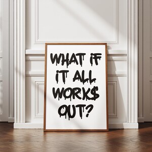 May include: A framed print with the text "WHAT IF IT ALL WORKS OUT?" in bold, dripping black letters. The print has a white background and a brown wooden frame. The artwork is displayed against a white wall and a wooden floor.