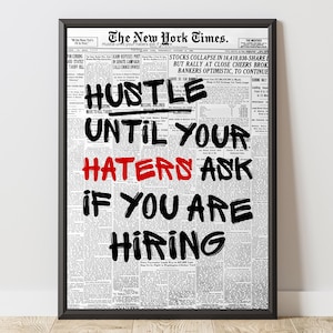 May include: Framed print featuring a vintage newspaper background with the headline "The New York Times." Bold text overlay reads "Hustle until your haters ask if you are hiring" in black and red.