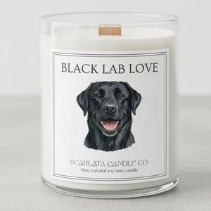Könnte beinhalten: Ein klares Glas-Kerzenglas mit einem Holzdeckel. Das Etikett trägt die Aufschrift "BLACK LAB LOVE" über einem Porträt eines schwarzen Labrador Retrievers. Auf dem unteren Teil des Etiketts steht "SCARLATA CANDLE CO." und "-10oz natural soy wax candle-".