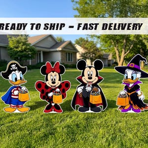 May include: Four cartoon character yard signs featuring a pirate duck, a ladybug mouse, a vampire mouse, and a witch duck. Each character holds a small orange candy bucket. The signs are displayed on a green lawn in front of a house.
