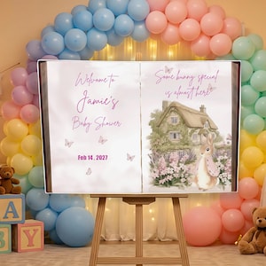 Może przedstawiać: Znak baby shower na sztaludze z napisem "Witamy na Baby Shower Jamie" i "14 lutego 2027". Prawa strona zawiera ilustrację królika z napisem "Specjalny króliczek jest prawie tutaj".