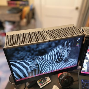May include: Two computer monitors with a zebra image on the screens. The monitors have a light brown, honeycomb-patterned cover. A small fan and remote control are visible below the monitors. A laptop is also visible.