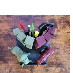 K&ouml;nnte beinhalten: Ein schwarzer Schreibtisch-Organizer mit einzigartigem Design, der Stifte, Scheren und farbige Bl&ouml;cke enth&auml;lt. Der Organizer verf&uuml;gt &uuml;ber zwei tierf&ouml;rmige Figuren in Gr&uuml;n und Burgunderrot. Der Schreibtisch-Organizer steht auf einer Holzoberfl&auml;che.