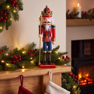 May include: A wooden nutcracker figurine wearing a red and blue uniform with gold accents, a crown, and a white beard. The figure holds a tall gold staff and stands on a rectangular red base, featuring painted details on the jacket and boots.
