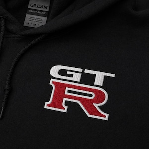 May include: Black hooded sweatshirt with the embroidered letters "GT" in white and the letter "R" in red. The sweatshirt has a drawstring and a tag that says "Gildan Heavy Blend".