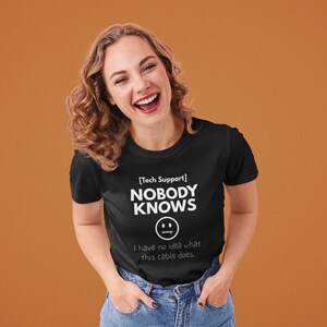 May include: Black t-shirt with the text "[Tech Support] NOBODY KNOWS" and a smiley face graphic. Below the graphic, the text reads "I have no idea what this cable does."