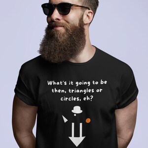 Può includere: T-shirt nera con la scritta "What's it going to be then, triangles or circles, eh?" e "ULTRA GEOMETRY" in arancione. La maglietta presenta un design geometrico con un cappello, un triangolo, un cerchio e una freccia. La persona nell'immagine indossa occhiali da sole.