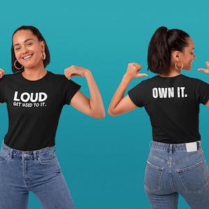 Könnte beinhalten: Schwarzes T-Shirt mit den weißen Worten "LOUD GET USED TO IT" auf der Vorderseite. Auf der Rückseite des Shirts steht "OWN IT". Das Model trägt eine blaue Jeans.