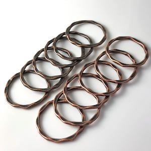 May include: A set of ten copper-toned metal rings with a hammered texture. The rings are stacked and overlapping, creating a decorative and rustic look.