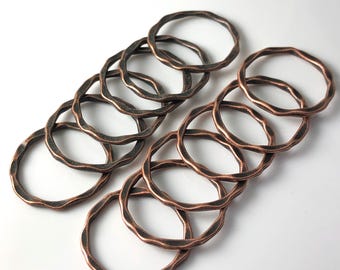 May include: A set of ten copper-toned metal rings with a hammered texture. The rings are stacked and overlapping, creating a decorative and rustic look.