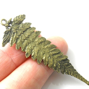 May include: A detailed, antique brass-colored fern leaf pendant. The pendant has a textured surface with intricate leaf details and a small loop at the top for hanging. The fern is a botanical design.