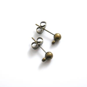May include: Two bronze-colored earring posts with small round balls at the end. The posts are designed to be inserted into the earlobe.
