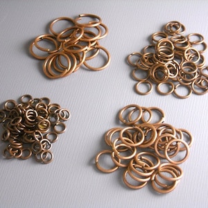May include: Four piles of copper jump rings of different sizes. The jump rings are used for jewellery making and crafting.