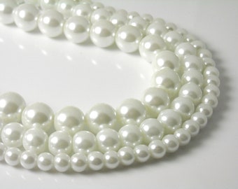 May include: A strand of white faux pearls of varying sizes, arranged in a circular pattern.