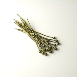 May include: A bunch of gold-toned head pins with round heads. The pins are arranged in a fan shape.