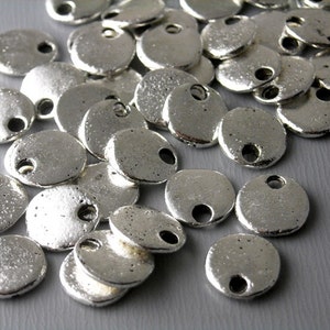 May include: A pile of silver-toned metal round charms with a hole in the center. The charms have a textured surface.