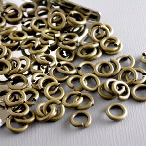May include: A large pile of antique brass jump rings. The rings are all the same size and are arranged in a random pattern.