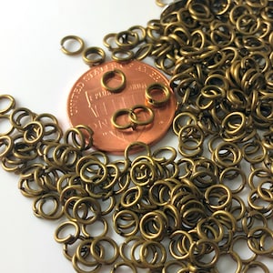 May include: A large quantity of small, gold-toned jump rings. The rings are approximately the size of a US penny.
