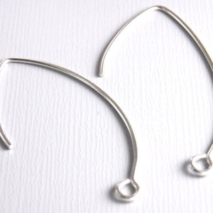 May include: Two silver earring hoops with a rounded opening at the bottom. The hoops are made of thin wire and are slightly oval shaped.