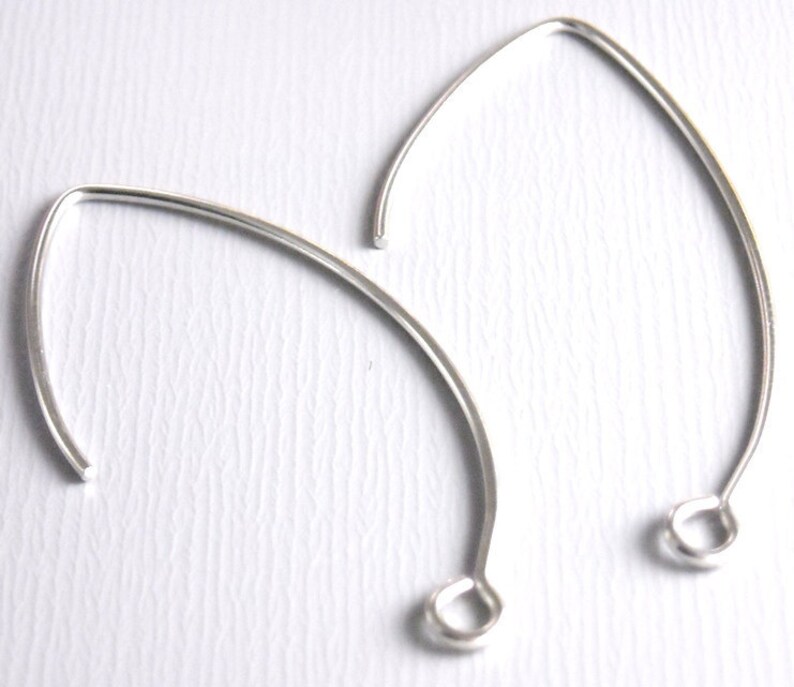 May include: Two silver earring hoops with a rounded opening at the bottom. The hoops are made of thin wire and are slightly oval shaped.