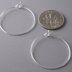 May include: A pair of silver hoop earrings, shown next to a US dime for size comparison. The hoops are simple and circular, with a hinged closure.