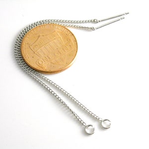 May include: Two silver chains with small silver loops at the ends. The chains are lying on a white surface next to a US penny.