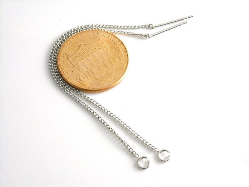 May include: Two silver chains with small silver loops at the ends. The chains are lying on a white surface next to a US penny.