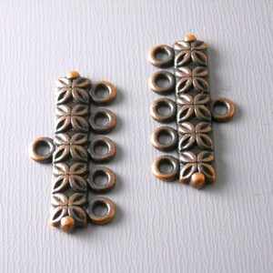 May include: Two antique copper-toned metal clasps with four loops each. The clasps have a decorative floral pattern.