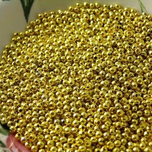May include: A bowl filled with small, round, gold-colored beads. The beads are shiny and have a metallic finish.