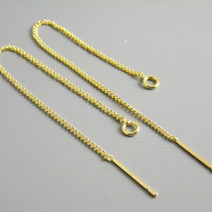 May include: A pair of gold chain earrings with a small loop at the top and a long, thin gold bar extending from the bottom.