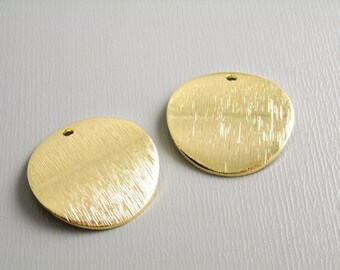 May include: Two gold-colored metal circles with a textured surface and a small hole at the top.