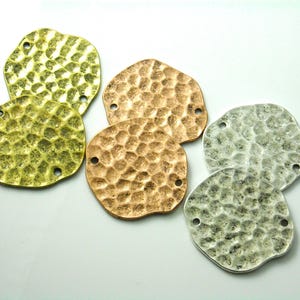 May include: A collection of six irregular, circular metal charms featuring a hammered, textured surface. The set includes two gold-toned, two copper-toned, and two silver-toned pieces, each with two small holes positioned on opposite sides.