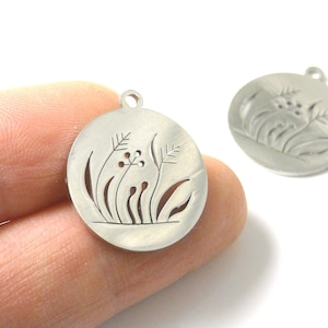 May include: Two silver metal charms with a cut-out design of a flower and leaves. The charms are round and have a hole at the top for attaching to a chain or bracelet.