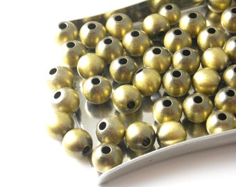 May include: A close-up of a tray filled with round, gold-colored metal beads. The beads have a matte finish and a small hole in the center.