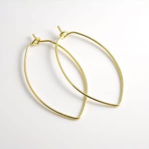 May include: A pair of gold-toned oval hoop earrings. The earrings are made of thin wire and have a simple, elegant design.