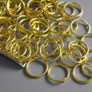 May include: A pile of gold-colored jump rings. The rings are small and round, and they are all piled on top of each other.