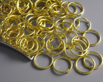 May include: A pile of gold-colored jump rings. The rings are small and round, and they are all piled on top of each other.